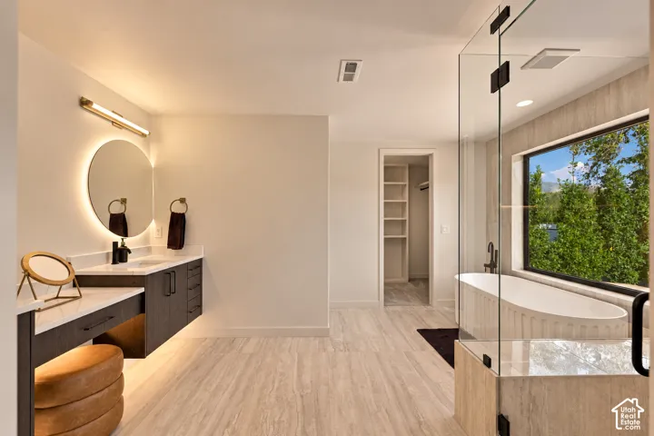 Floating dual-tone vanity with a stone countertop, backlit circular mirror, floor-to-ceiling glass-enclosed shower, freestanding soaking tub, and stone-finish flooring