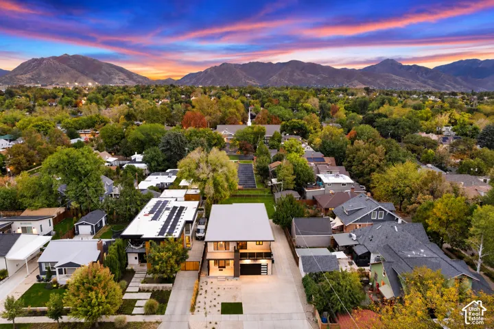 Aerial perspective featuring a two-story residence with a flat roof, integrated garage, upper-level balcony, and mountain backdrop