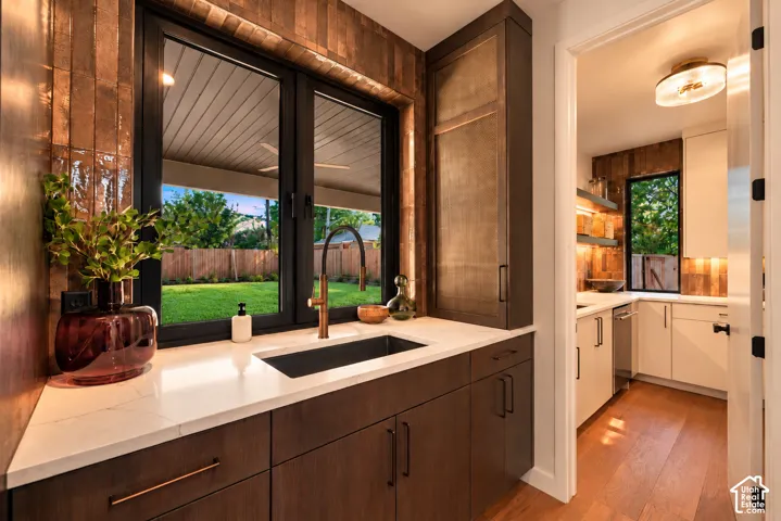 Custom cabinetry with metallic-finish detailing, quartz countertop, dark-finish undermount sink with arched faucet, and textured tile wall surround