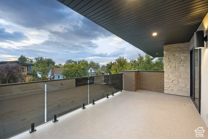 Covered outdoor balcony featuring a glass panel railing, textured flooring, natural stone veneer siding, and a dark-toned tongue-and-groove ceiling