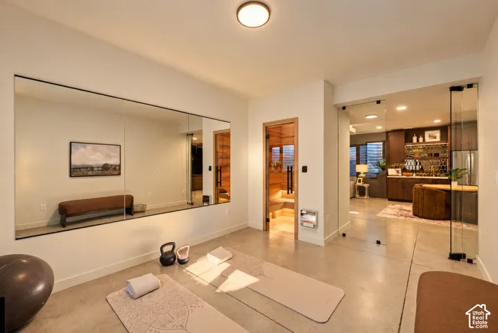 Expansive room featuring polished concrete flooring, a wall-mounted mirrored panel, a wood-lined sauna with a glass door, and a full-height glass partition wall