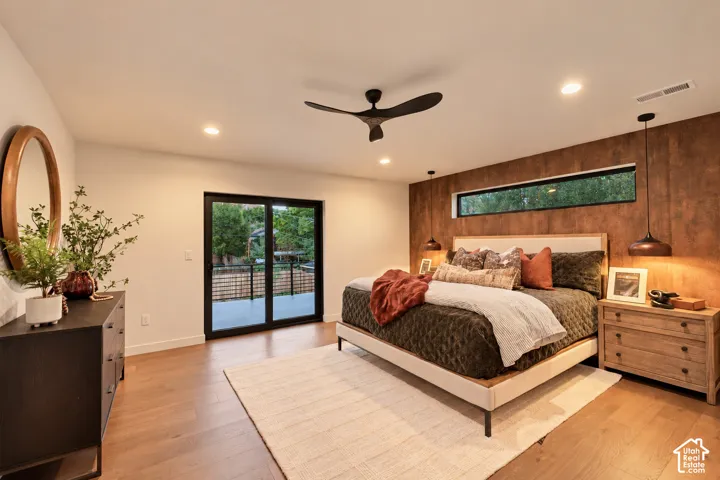Room featuring wood-finish flooring, a textural wood-panel accent wall, recessed lighting, a multi-blade ceiling fan, and sliding glass doors