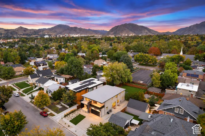 Aerial perspective of a multi-story residence featuring a flat roof, solar panel array, attached garage, and private lawn area, set against a prominent mountain backdrop