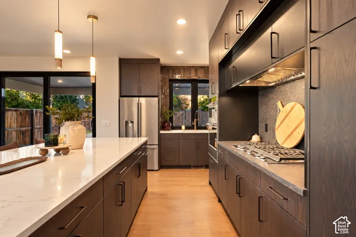 Kitchen featuring dark wood-finish cabinetry, a large stone-topped island, gas cooktop with integrated range hood, built-in wall oven, and recessed lighting