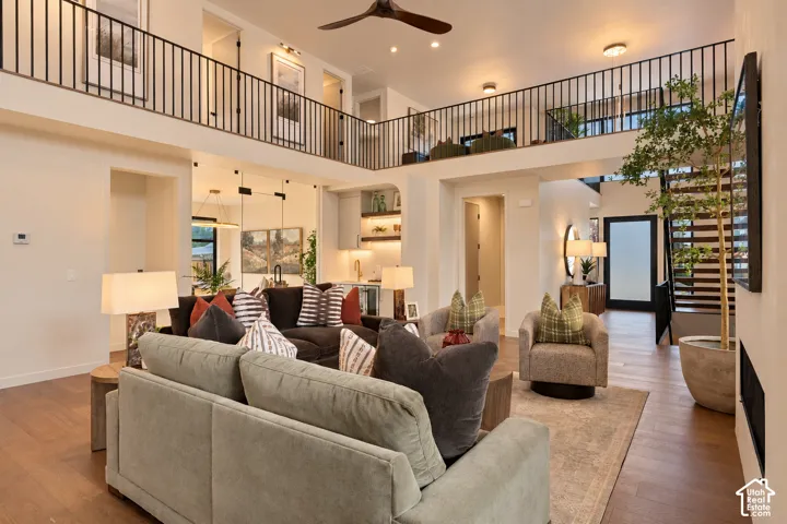 Open-concept interior featuring double-height ceilings, a mezzanine with black metal railing, wood-finish flooring, a built-in wet bar, and a flush-mounted fireplace