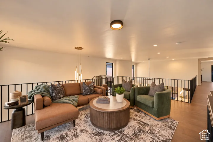 Open-concept interior featuring wood-finish flooring, matte black metal railings, recessed lighting, and a multi-tiered contemporary pendant light fixture