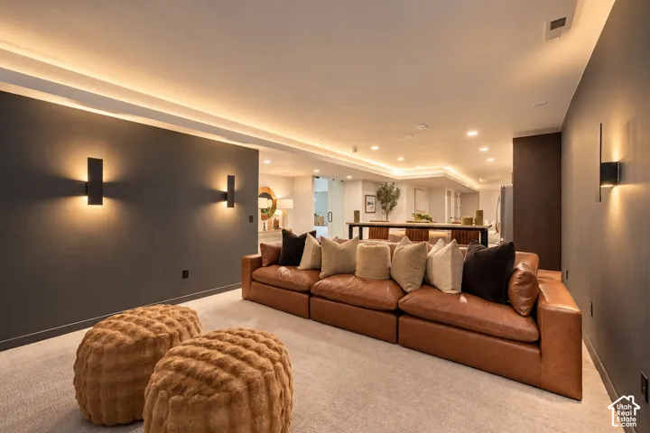 Living area featuring recessed cove lighting, dark charcoal accent walls, modern wall-mounted sconces, and neutral carpeting
