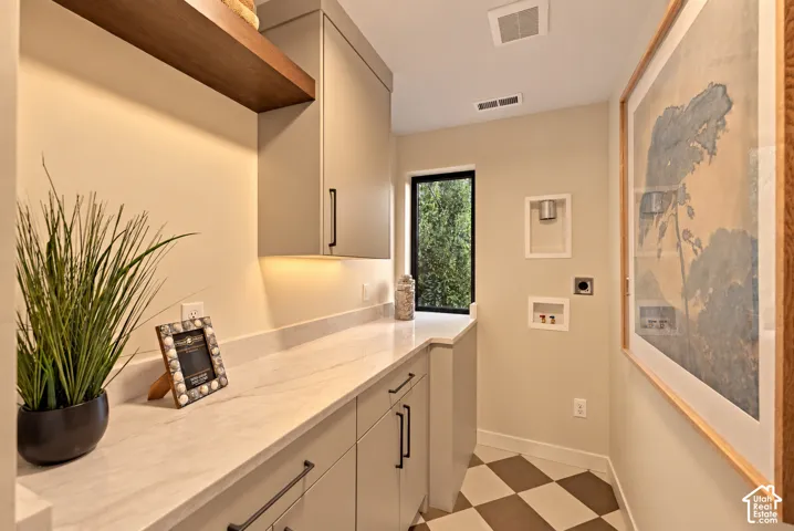 Laundry room featuring solid-surface countertops, custom cabinetry, under-cabinet lighting, a floating wooden shelf, and a checkered floor pattern