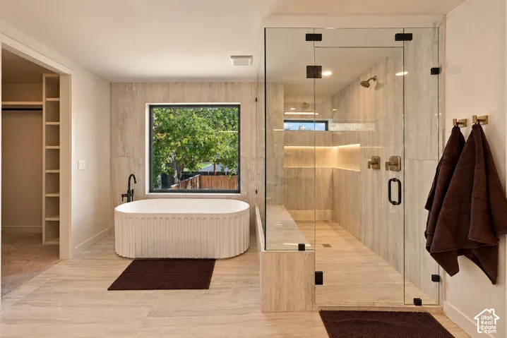Freestanding ribbed soaking tub, large walk-in glass-enclosed shower with tiled bench, recessed niche lighting, and stone-finish floor tiling