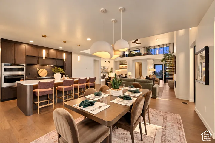 Open-concept kitchen featuring dark cabinetry, a large kitchen island with quartz countertops, built-in stainless steel wall ovens, wood-finish flooring, and sculptural pendant lighting