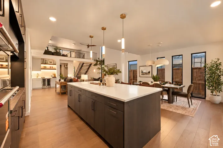 Kitchen featuring a large central island with quartz countertops, dark cabinetry, wood-finish flooring, metal pendant lighting, and vertical window arrays