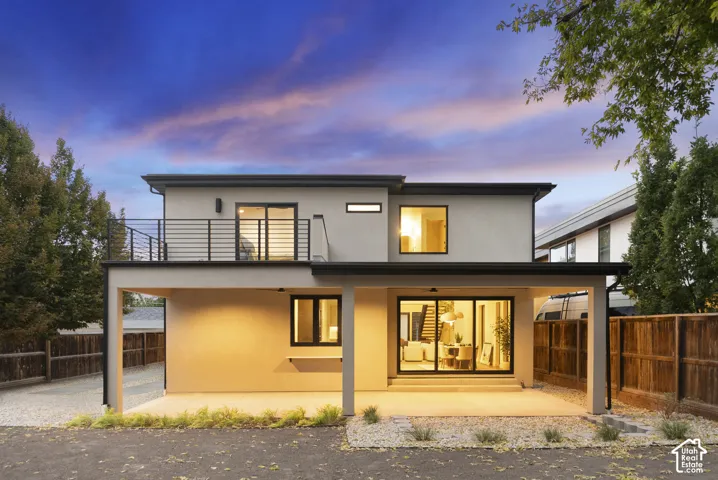 Two-story exterior featuring smooth stucco siding, a covered concrete patio, a second-story balcony with metal railing, and large-format sliding glass doors