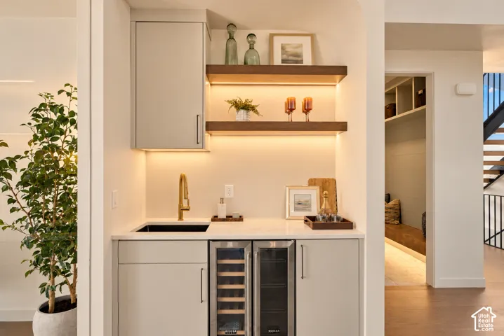 Built-in wet bar featuring stone-finish countertops, custom cabinetry, brass-finish faucet, dual-zone wine refrigeration, and wood-finish floating shelves with integrated lighting