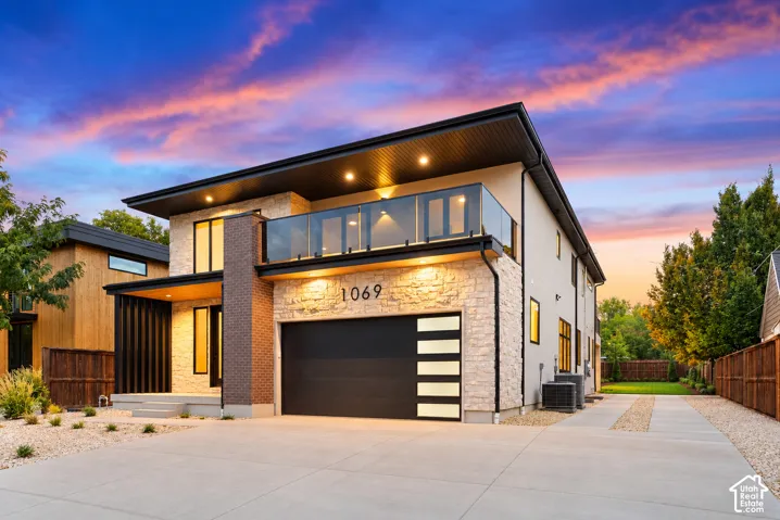 Contemporary exterior featuring natural stone veneer, a glass-railed second-story balcony, vertical dark brick accents, and a modern garage door with frosted horizontal windows