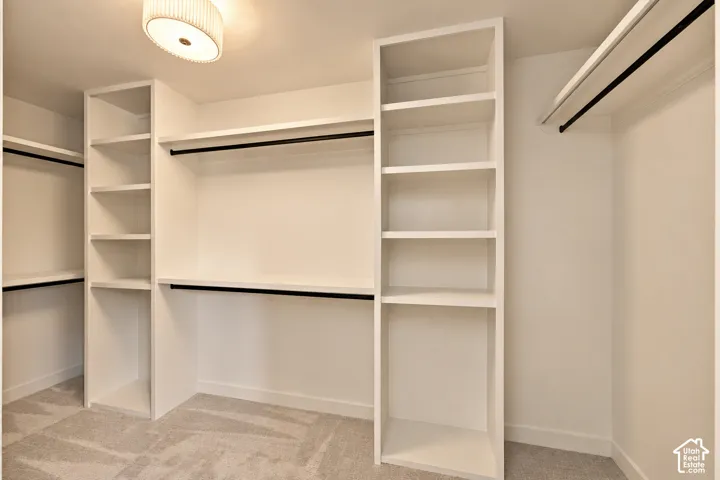 Custom-built white cabinetry featuring multiple shelving units and integrated clothing rods, accompanied by neutral carpeting and a drum-style ceiling light fixture