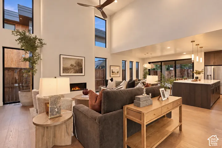 Double-height living area featuring floor-to-ceiling windows, linear gas fireplace, wood-finish flooring, and a kitchen island with stone countertop