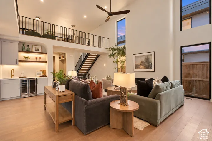 Double-height living area featuring floor-to-ceiling windows, built-in wet bar with under-cabinet lighting, wood-finish flooring, and an open mezzanine with metal railing