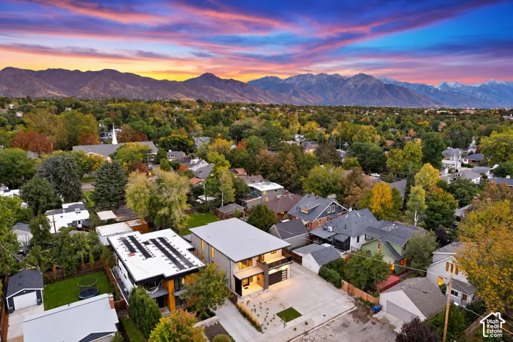 Aerial perspective of a multi-story residence featuring a flat roofline, attached balcony, private concrete driveway, and expansive mountain backdrop