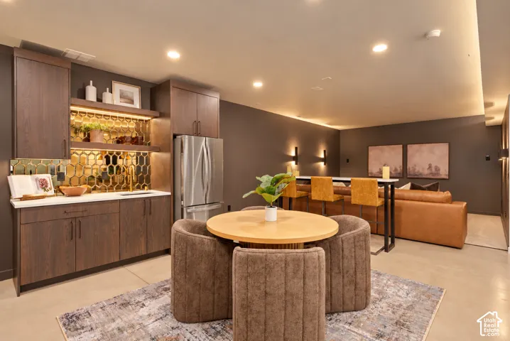 Wet bar featuring custom dark wood cabinetry, metallic honeycomb backsplash, and integrated under-cabinet lighting, complemented by recessed ceiling lights and concrete flooring