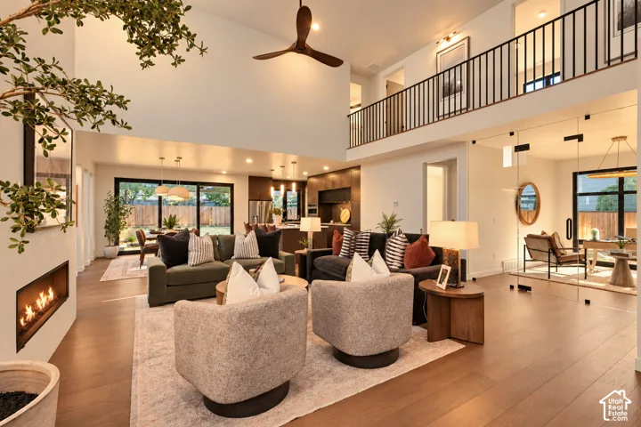 Open-concept interior featuring double-height ceilings, linear fireplace, dark wood-finish flooring, metal staircase railing, and glass-enclosed partitioned space