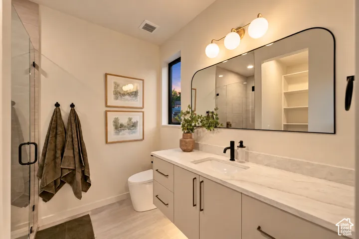 Floating vanity with stone countertop, rectangular undermount sink, matte black hardware, arched wall mirror, and glass-enclosed shower