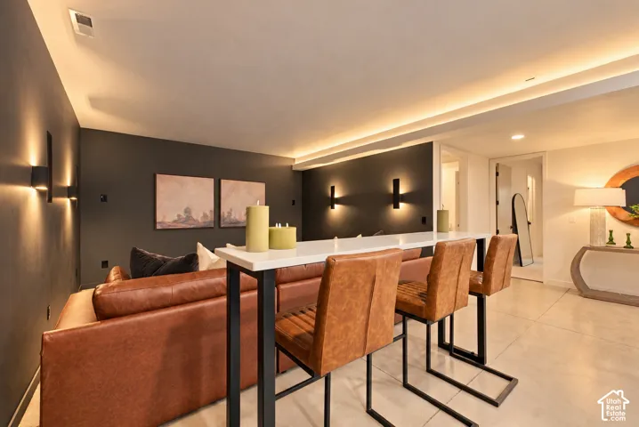 Contemporary room featuring large-format tile flooring, matte dark accent walls, recessed cove lighting, and structured wall-mounted sconces