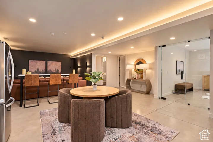Open-concept space featuring polished concrete flooring, recessed ceiling lighting with cove illumination, wall-mounted accent lighting, and an expansive glass-enclosed room