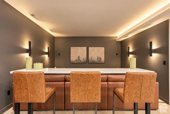 Built-in bar with a solid surface countertop, cove ceiling lighting, and matte black wall-mounted sconces
