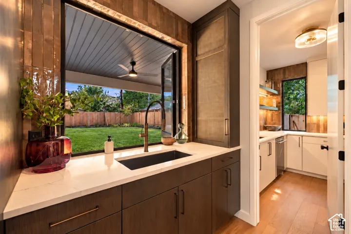 Kitchen featuring a pass-through window with folding glass doors, dark wood cabinetry, a matte black undermount sink with a bronze-finish faucet, and light-toned stone countertops