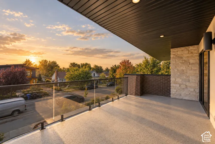 Covered balcony featuring a glass panel railing, recessed ceiling lighting, textured stone accent wall, and dark brick exterior cladding