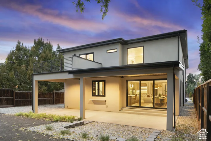 Two-story exterior featuring smooth stucco siding, a covered concrete patio, a second-story balcony with metal railing, and large sliding glass doors