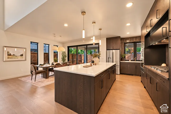 Kitchen featuring a substantial island with stone surfacing, dark wood-finish cabinetry, recessed ceiling lighting, three cylindrical pendant fixtures, and wood-finish flooring