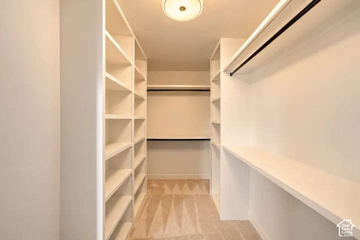 Walk-in closet featuring extensive built-in white shelving, integrated hanging rods, flush-mount ceiling lighting, and wall-to-wall carpeting