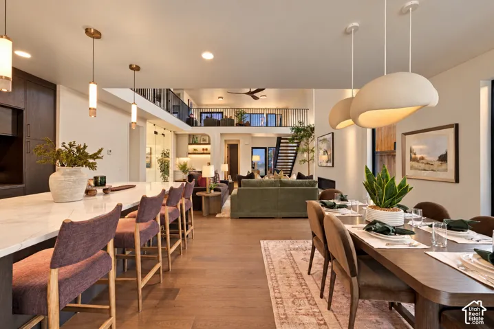 Open-concept living space featuring wood-finish flooring, a kitchen island with stone-surface countertop, bespoke pendant lighting, and a prominent balcony with metal railing