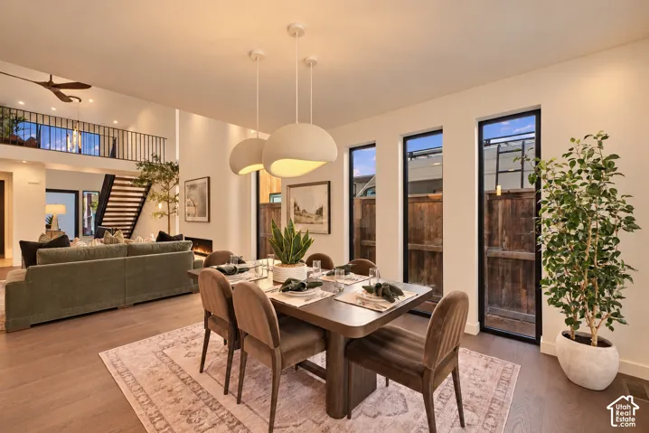 Open-concept interior featuring tall ceilings, wood-finish flooring, dual-tone contemporary pendant lighting, floor-to-ceiling windows, and a metal-railed staircase