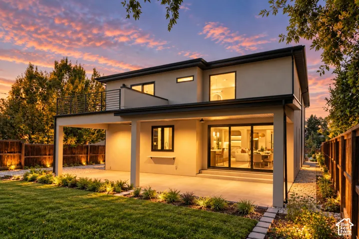 Two-story exterior featuring smooth stucco siding, a covered concrete patio, an upper-level balcony with metal railings, and sliding glass doors