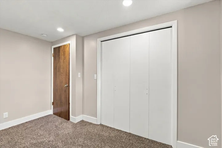 Interior space featuring neutral wall paint, wall-to-wall carpeting, recessed ceiling lighting, a wood-finish interior door, and a white bifold closet door