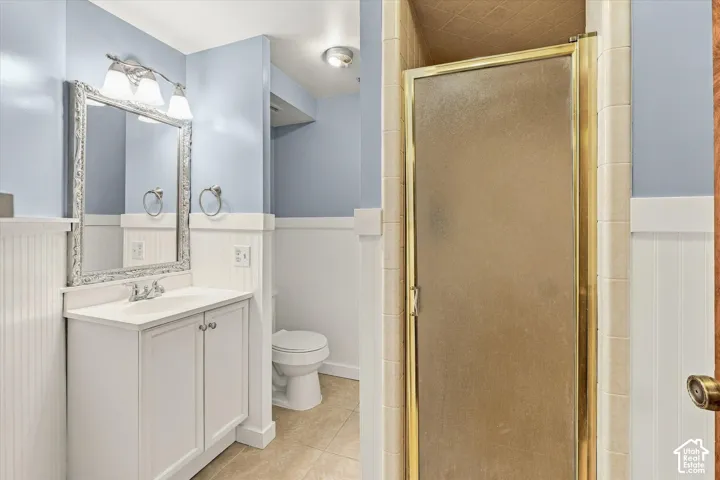 Bathroom featuring beadboard wainscoting, white vanity with integrated sink, shower enclosure with brass-tone frame, and tile flooring