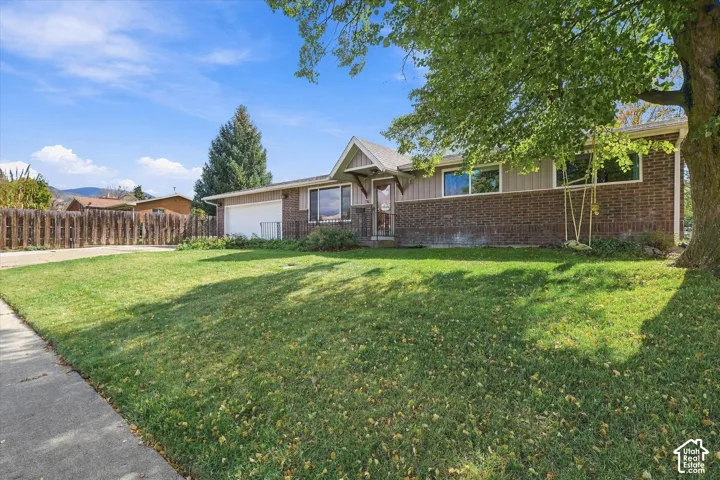 Ranch-style exterior featuring a brick facade, vertical siding, attached garage, and mature landscaping