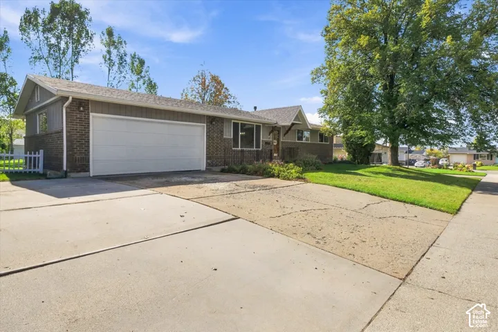 Single-level exterior featuring a multi-material facade of brick and vertical siding, attached two-car garage, concrete driveway, and mature landscaping