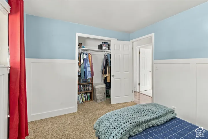 Bedroom featuring white wainscoting, neutral carpeting, and a built-in closet with six-panel door