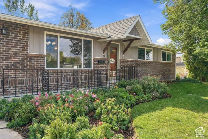 Exterior featuring a brick and vertical siding facade, gabled roofline over the entryway, iron railings, and landscaped flower beds