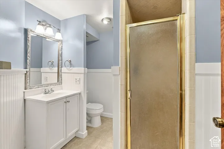 Bathroom featuring white wainscoting, a vanity with a white countertop and basin, a framed wall-mounted mirror, and a tiled shower enclosure with metal trim