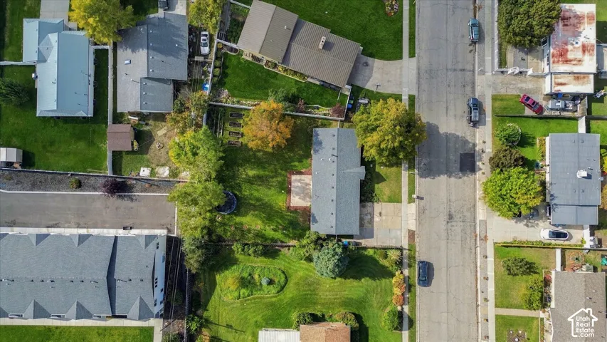 Aerial perspective featuring a residential lot with a paved driveway, a concrete rear patio, mature trees, and landscaped lawn