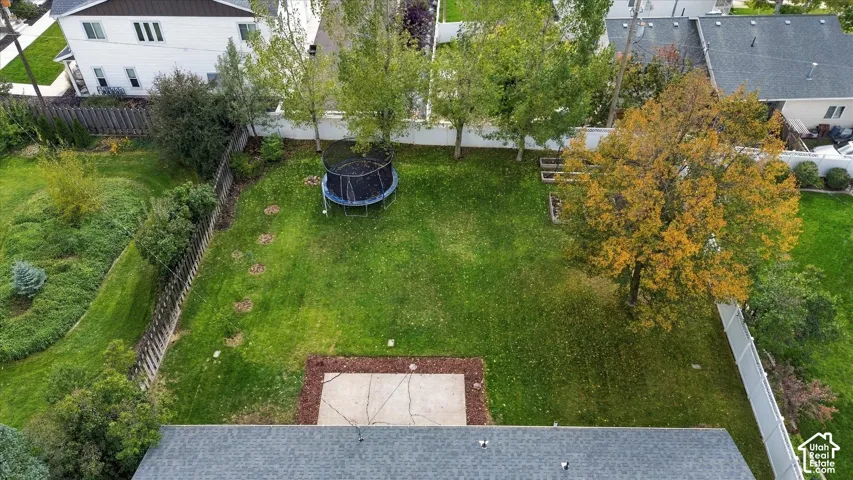 Fenced backyard featuring a concrete patio, mature trees, and designated planting beds