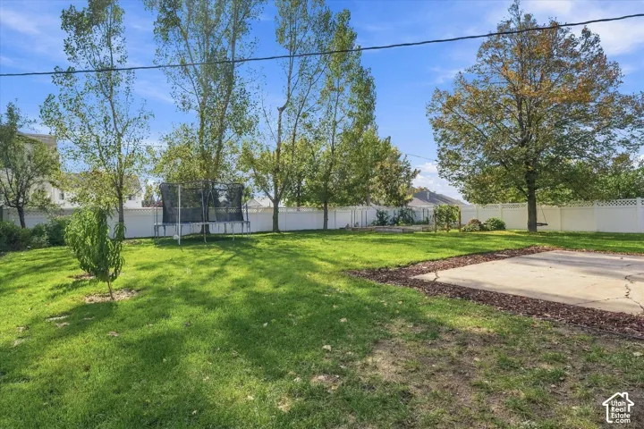Spacious backyard featuring a large grass lawn, perimeter vinyl fencing, mature trees, and a concrete patio pad