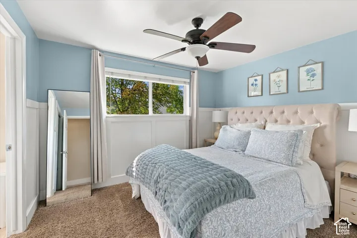 Room featuring wainscoting, ceiling fan, carpeted flooring, and a window with exterior scenery