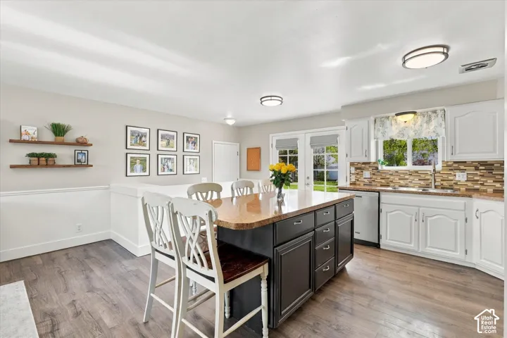 Kitchen featuring white cabinetry, a center island with built-in storage, wood-finish flooring, multi-colored stone-tile backsplash, and glass-paneled double doors