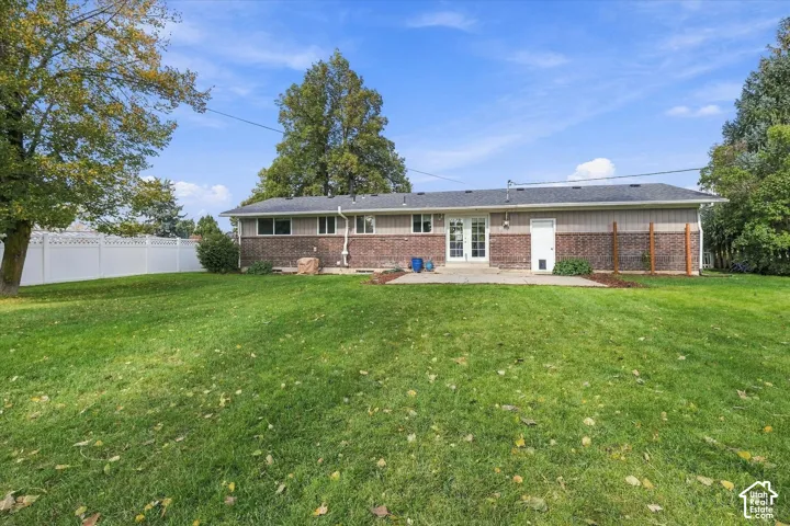 Expansive backyard featuring a manicured lawn, concrete patio, brick and siding exterior, and a white privacy fence