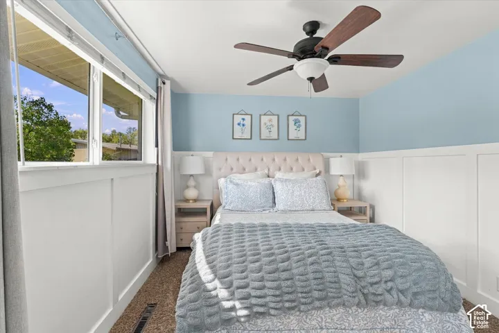 Room featuring white wainscoting, a multi-blade ceiling fan with integrated lighting, and neutral carpeting